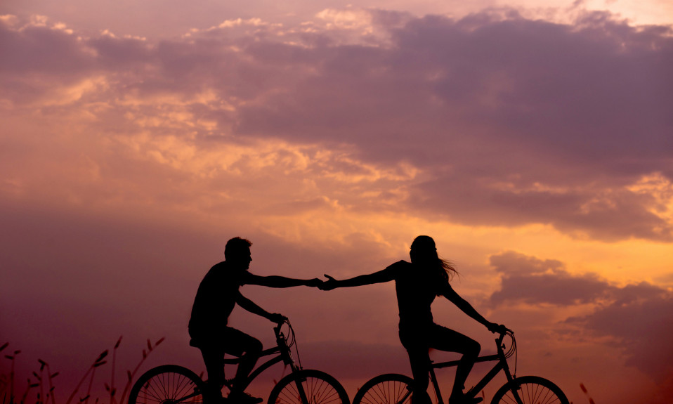 Two individuals on separate bicycles holding hands.